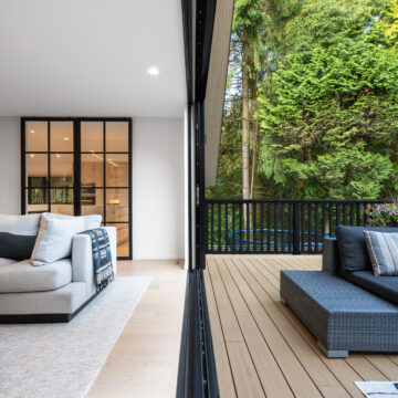 North Vancouver Renovation Seamless Indoor-Outdoor Living with Sliding Glass Wall Open-concept transition from a cozy modern living room to a forest-facing deck, with sliding glass doors, black framed French interior doors, and sleek outdoor seating overlooking lush greenery.