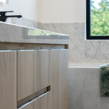 North Vancouver Renovation of a Primary Ensuite Custom Vanity North Vancouver close-up of a modern bathroom featuring a double sink vanity with light wood cabinetry, white countertops, matte black faucets, and a large wall-mounted mirror reflecting a clean, minimalist design.