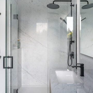 North Vancouver Primary Ensuite Renovation with Floor to Ceiling Marble North Vancouver elegant primary ensuite renovation featuring a glass-enclosed walk-in shower with full-height marble-look porcelain walls, dual matte black rain showerheads, a matching faucet, and a sleek vanity with a white countertop.