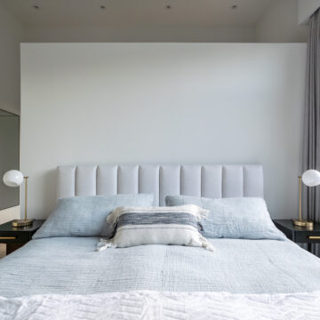 North Vancouver Minimalist Primary Bedroom Design Close-up of a serene bedroom featuring a vertical tufted headboard, soft blue-grey bedding, layered accent pillows, and modern globe table lamps on black nightstands, set against a clean white backdrop renovation in North Vancouver.