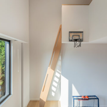North Vancouver Kid's Loft Custom Ladder Stairs Bright and playful double-height kids’ bedroom featuring a wood loft ladder, built-in loft platform, mini basketball hoop, and a hockey net with balls, with sunlight streaming in through a large window.