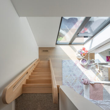 North Vancouver Home Renovation Kid's Room View From Loft with Custom Ladder Bird's-eye view from a loft space showing a light wood staircase leading into a kids’ bedroom filled with natural light from a large skylight, colorful toys, and a patterned rug on wood flooring.