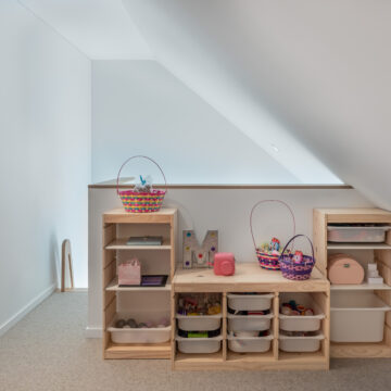 North Vancouver Renovation of Kid's Third Floor Loft with Storage North Vancouver Charming loft play space tucked under a sloped ceiling, featuring light wood open shelving units with labeled storage bins and baskets, perfect for organizing toys and creating a playful nook in a child’s bedroom.