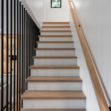 North Vancouver Home Renovation Custom Oak Staircase traight staircase featuring light wood treads, white risers, a natural wood handrail, and a sleek black vertical slat railing, leading to the upper floor of a contemporary home with minimalist design.
