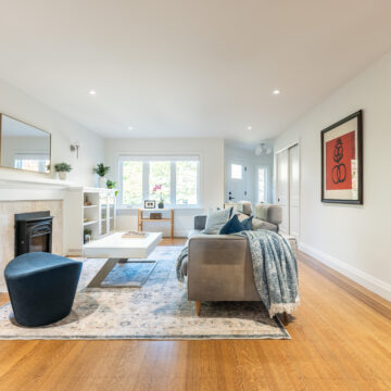 Open living room renovation featuring a classic fireplace with custom built-in shelving, light wood flooring, neutral furnishings, layered rug, and large windows bringing in natural light.