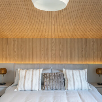 Custom primary bedroom featuring a wood slat ceiling and matching feature wall, integrated LED backlighting, upholstered headboard, and symmetrical bedside tables with warm ambient lighting.