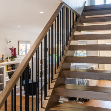 Close-up of a floating oak staircase featuring open risers, solid wood treads, and black steel balusters overlooking a refined living space.